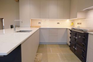 Modern kitchen with light grey and purple cabinetry, a sleek worktop and a dark stove. A bright and minimalist design.