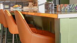 Details of the brass worktop on the island and orange bar stools.