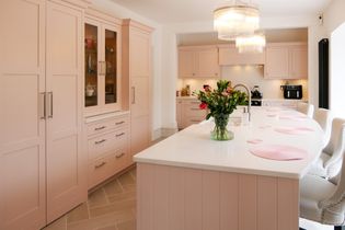 Large pink island with pink placemats and flowers next to the tap. Sink sits in the island with surrounding pink cabinetry.