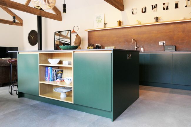 A modern kitchen with an island featuring open shelving, green cabinetry, and wooden accents.