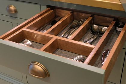 Open wooden drawer with an oak cutlery insert in a olive green bespoke kitchen