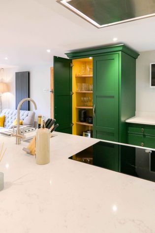 Shaker kitchen with a sleek white countertop, an integrated stove, and a green cabinet with open doors revealing glassware. Cozy seating area visible.