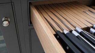 Open kitchen drawer with organized knives in a wooden block, handles outwards. The setting is sleek and modern, with a grey cabinet.