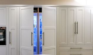 A Shaker kitchen with off white cabinetry and an open refrigerator in the centre, displaying its contents.