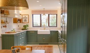 A Shaker kitchen with green cabinetry, a large farmhouse sink, and a window overlooking a garden.