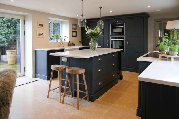 Dark Shaker kitchen with white worktops, potted house plants and a vase of white lilies in the centre of the island.