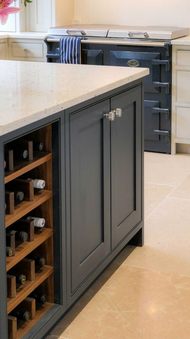 Stylish kitchen with a navy island featuring wine storage on the side. In the background, a navy range cooker with a striped towel adds a cozy touch.