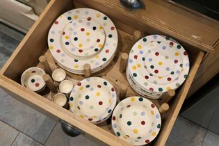 Open wooden drawer with neatly stacked polka-dot plates and bowls in various sizes. Bright colours evoke a cheerful, organised kitchen setting.
