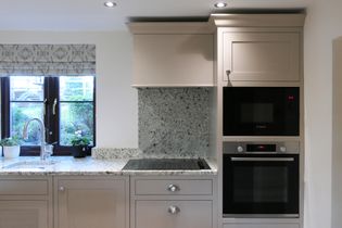 Shaker kitchen with neutral cabinets, integrated hob, wall ovens, and a window with potted plants providing natural light.