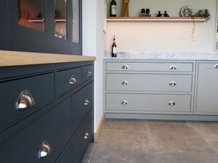 Shaker kitchen space with gray and dark cabinets, silver handles, a shelf with bottles, and a granite countertop, conveying a modern, clean vibe.