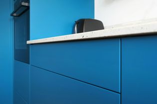 Modern kitchen featuring a close up of bright blue cabinets and drawers, a white speckled countertop, and a black toaster. The scene is sleek and contemporary.