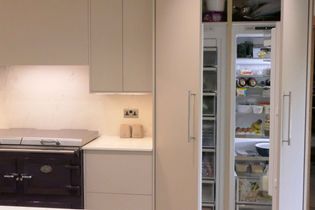 Modern kitchen with light grey cabinets, a black stove, and an open fridge showing organized shelves with food items. Clean, functional, and inviting.