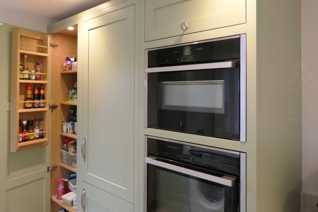 Shaker kitchen with an open pantry door revealing shelves stocked with spices and staples; adjacent double ovens convey a sleek, organized ambiance.