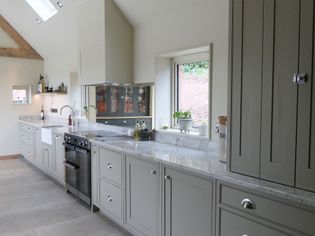 Bright kitchen with light gray cabinets, granite countertops, and a large window. The space feels modern and airy, accented by plants and clean lines.