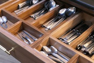 Open wooden cutlery drawer with organised compartments; neatly arranged forks, knives, and spoons in silverware sections, conveying tidiness.