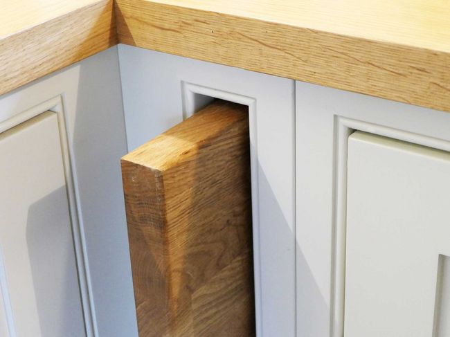 A hidden wooden drawer extends from a white kitchen cabinet against a wood countertop. The elegant design showcases seamless storage integration.