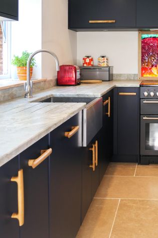 Close up of navy blue kitchen with solid oak bar handles, granite worktop and exposed front sink