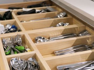 Wooden drawer organizer filled with neatly arranged silverware, including forks, knives, and spoons. Bright, tidy kitchen setting.