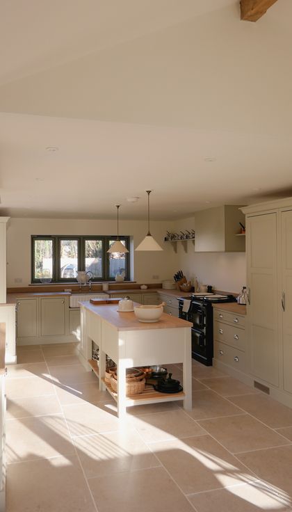 A Shaker kitchen with light-coloured cabinets, a large wooden countertop, a sink, and an AGA stove. There are utensils and kitchen tools neatly arranged, along with a window allowing natural light to fill the space.