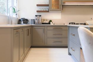Grey kitchen cabinets with sleek brass handles under a white countertop. The design is modern and minimal, conveying a clean, elegant tone.