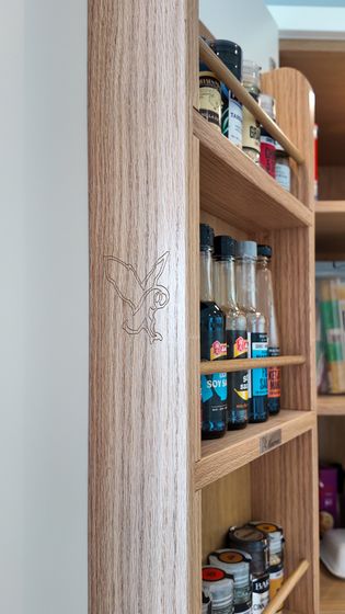 A close-up of a wooden shelf containing various bottles of sauces and spices, with a decorative engraving on the corner.
