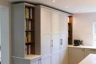 Modern kitchen with white cabinets, recessed shelves filled with colorful books, and a coffee machine on a sleek countertop. Bright and organized space.