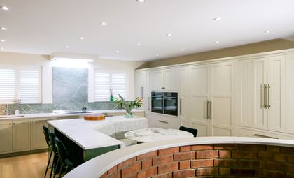 A neutral Shaker kitchen with cream cabinetry, a marble style splash back, a central island with bench seating.