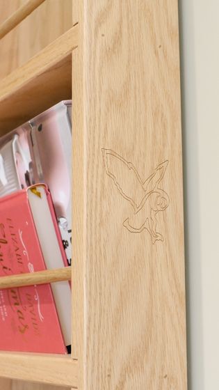 A close-up of a wooden shelf with an etched bird design on the side, alongside visible book spines.