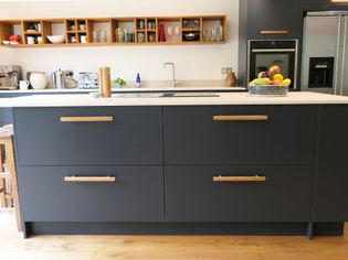 Large dark blue pan drawers on the side of the island with oven behind and wooden shelving on the wall