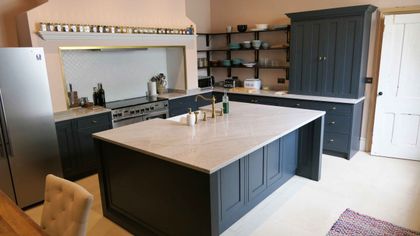 Shaker kitchen with dark blue cabinetry, open shelves, and a large pale stone island with a brass faucet.