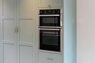 Shaker kitchen with sleek built-in oven and light green cabinets. Minimalist handles and soft lighting create a clean, contemporary look.