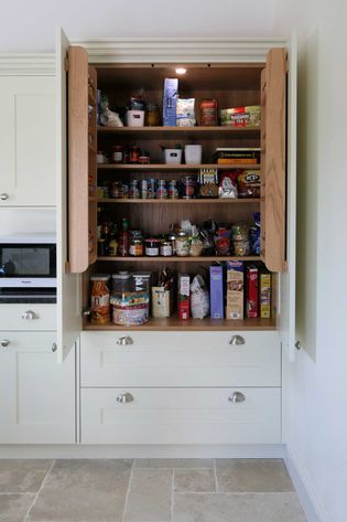Open kitchen pantry filled with assorted food items like cereals, canned goods, sauces, and snacks. Shelves neatly organized, light overhead enhances visibility.