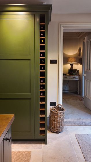 Shaker tall cabinet door with wine racking down the right hand side, a wicker basket sits to the right and a lamp in the background.