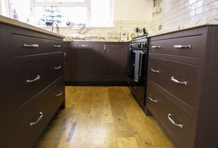 A Shaker kitchen with dark red cabinets and wooden flooring, featuring a stove and sink.