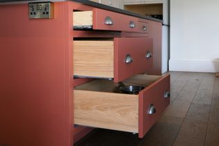 Shaker kitchen island with red-brown cabinets with multiple drawers open, revealing light wood interiors and a metal pan.