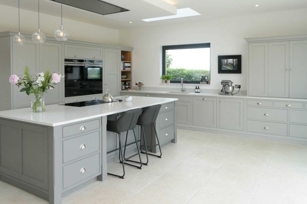 Shaker style grey and white kitchen with a large island, two bar stools, flowers, pendant lights, and a window overlooking greenery.
