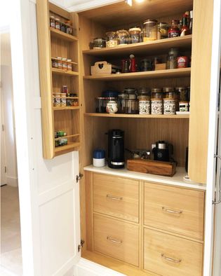 Wooden pantry with open shelves displaying jars of spices, grains, and a coffee machine. Warm tones and organized layout create a cozy, tidy feel.