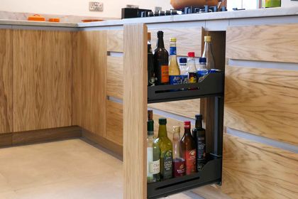 Pull-out corner storage rack holding bottles in oak handleless cabinetry