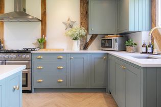 Rustic kitchen with blue cabinets, brass handles, and white countertop. Decor includes star ornaments, flowers, and a woven plant basket. Cozy atmosphere.