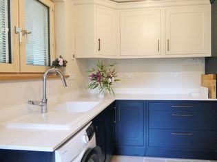 Shaker kitchen with white and navy cabinets, a silver faucet, and a white countertop. A vase with purple flowers adds a touch of elegance and freshness.